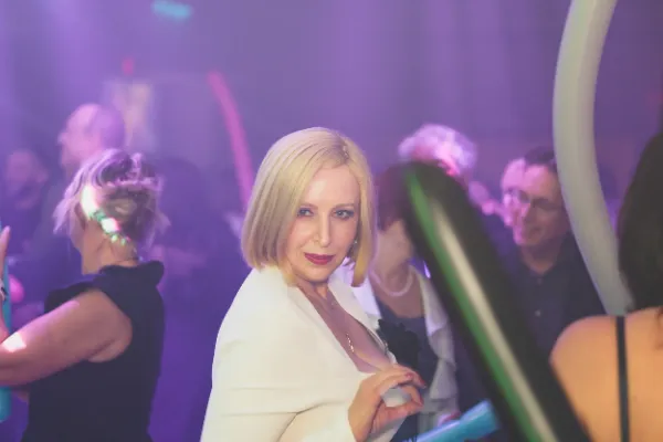 Blonde woman white blazer dancing crowd purple lighting