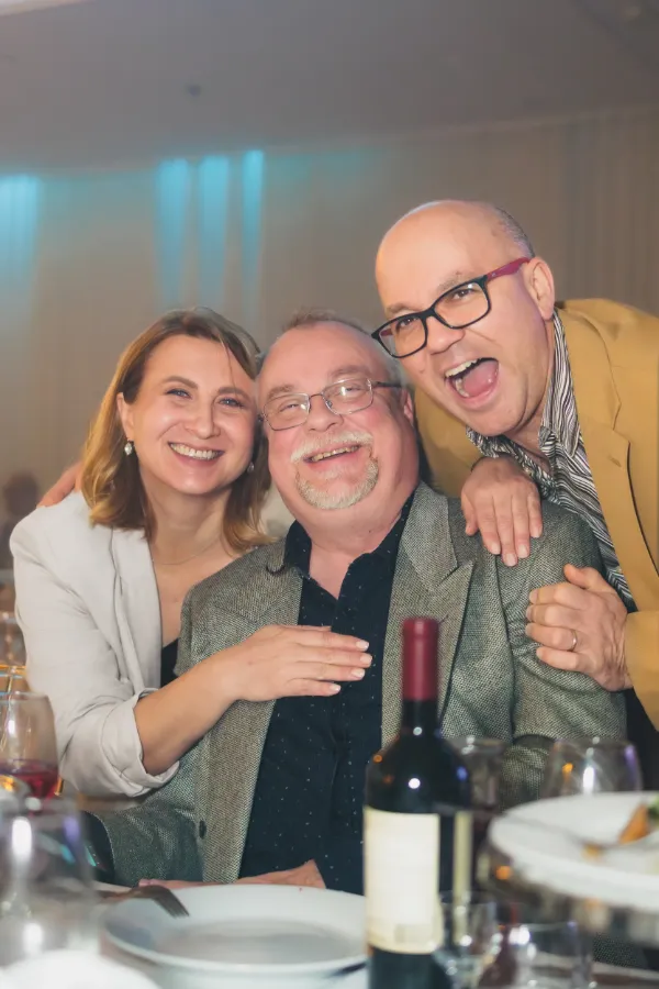 Three guests laughing hugging at table