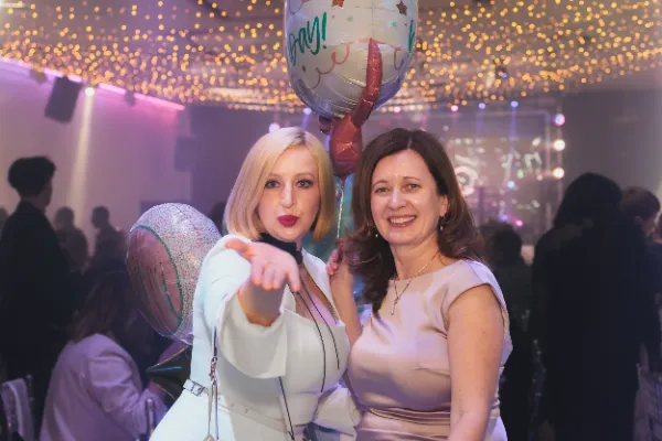 Two women birthday balloons pointing camera