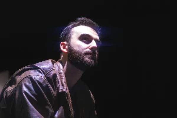 Actor in a leather jacket under dramatic side lighting on a film set