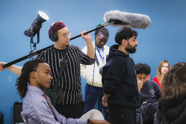 Bts boom operator holding mic over actors blue wall