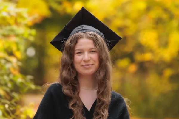 Grad girl black dress mortarboard subtle smile headshot autumn