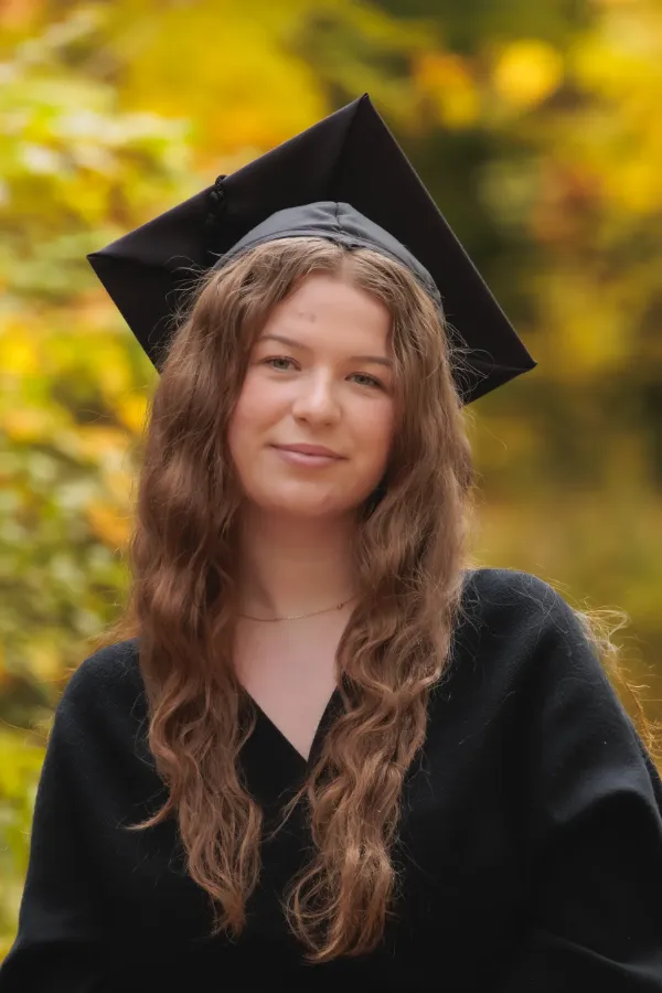 Grad girl black dress mortarboard tilted soft smile autumn