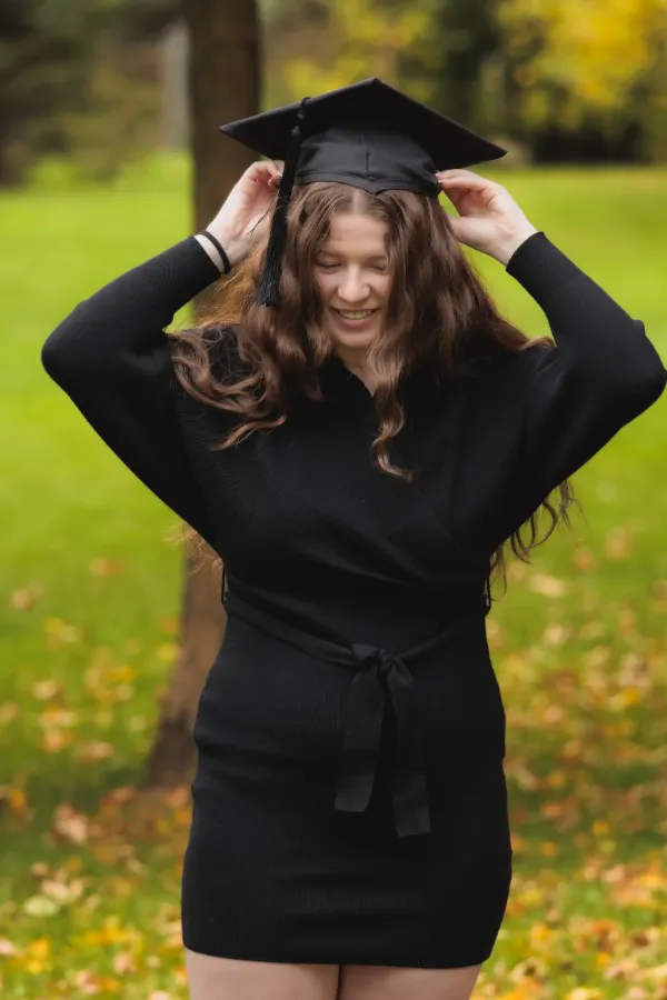 Grad girl black wrap dress adjusting mortarboard laughing