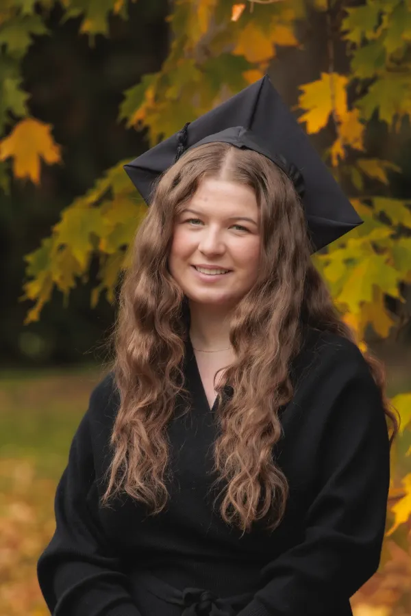 Grad girl black wrap dress mortarboard smiling under maple