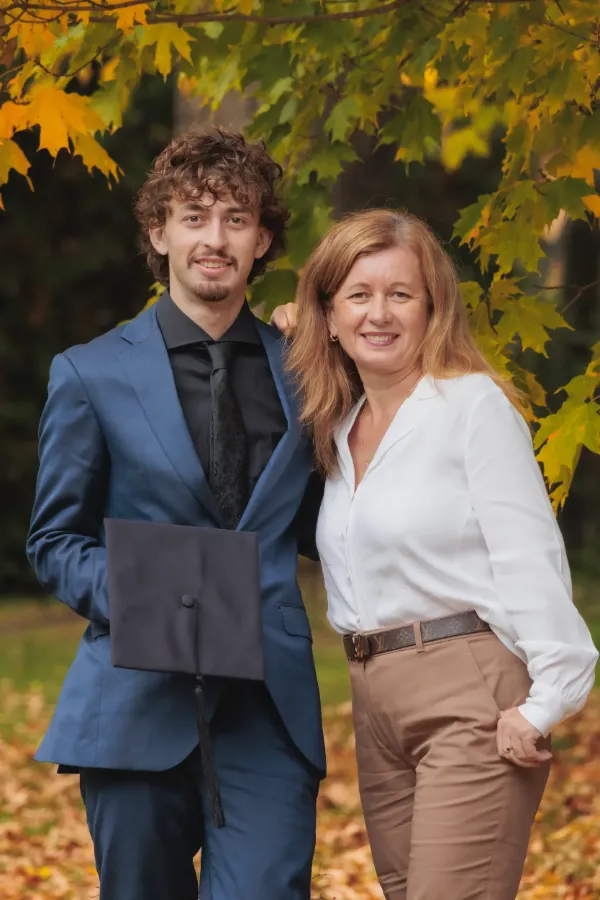 Grad guy and mom holding mortarboard under maple tree