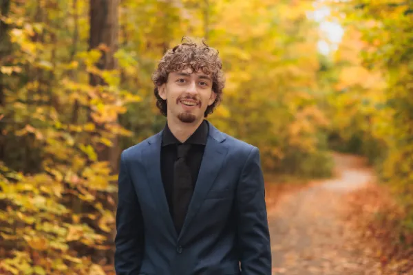 Grad guy blue suit big smile headshot autumn path bokeh