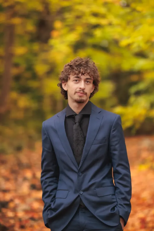 Grad guy blue suit half body smiling autumn leaves