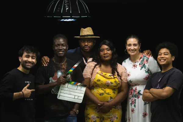 Full cast and crew group photo with clapperboard in a dark studio