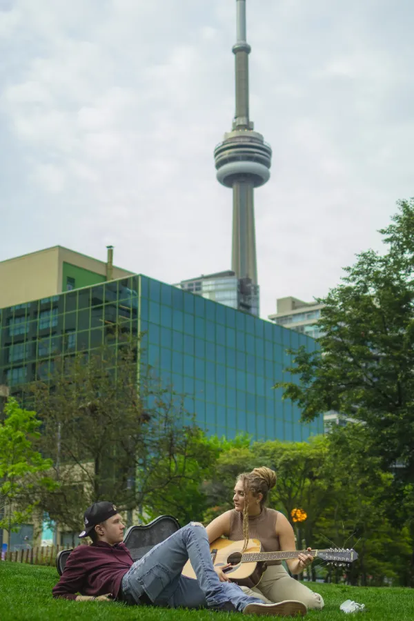 Two actors on grass female playing guitar cn tower toronto skyline