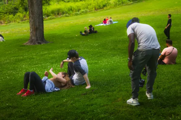 Director filming two actors lying sitting on park lawn