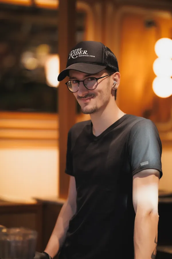 Young man black cap glasses earbuds restaurant warm light
