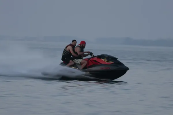 Two men red black jet ski speeding lake overcast