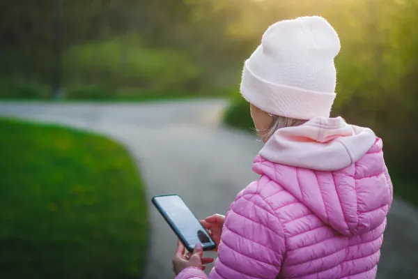Woman pink jacket white toque back view phone park path golden hour