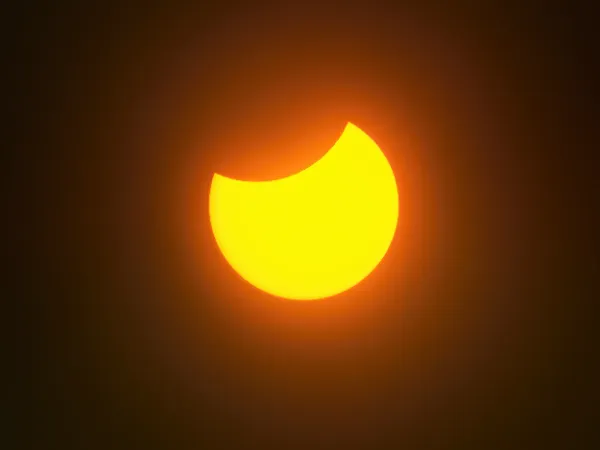 Solar eclipse partial moon covering upper right sun orange yellow