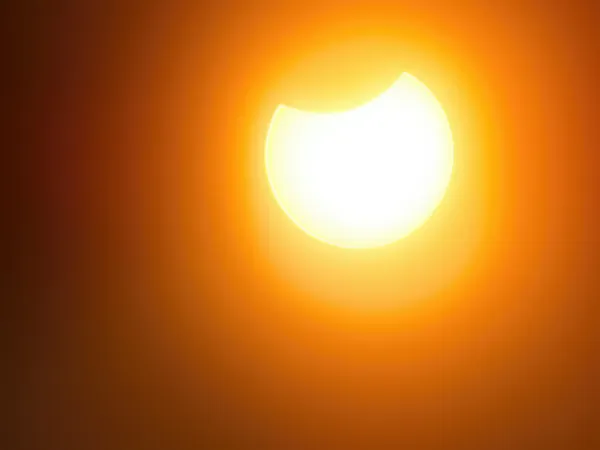 Solar eclipse partial moon covering upper right sun white core orange sky
