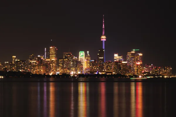 Toronto skyline at night with CN Tower pride lighting reflecting on the lake